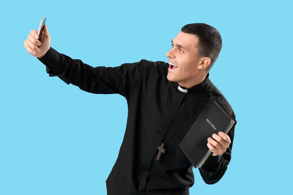 Young Priest Holy Bible Taking Selfie Blue Background — Stock Photo, Image