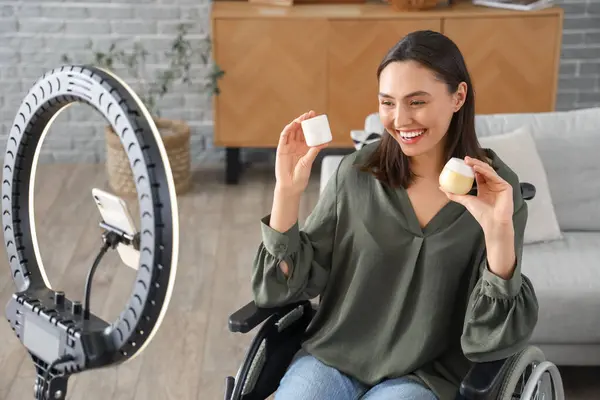 Female blogger in wheelchair with jars of cream recording video at home
