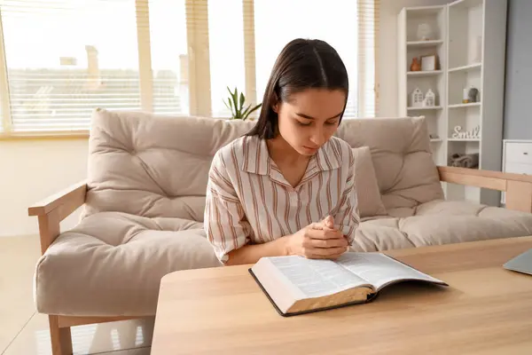 Beautiful young woman reading Bible and praying at home