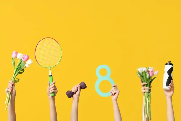 Female hands with paper figure 8, sports equipment and tulips for International Women's Day on yellow background