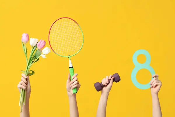 Female hands with paper figure 8, sports equipment and tulips for International Women\'s Day on yellow background