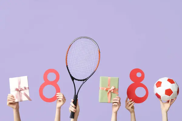 Female hands with paper figures 8, sports equipment and gifts for International Women's Day on lilac background