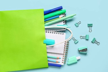 Mavi arka planda farklı okul kırtasiyesi olan yeşil alışveriş çantası.