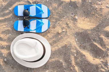 Renkli parmak arası terlikleri ve kumlu arka planı olan şık güneş gözlükleri.