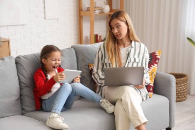 Çalışan genç bir kadın evde tablet bilgisayarlı gürültücü küçük kızı yüzünden stresli.