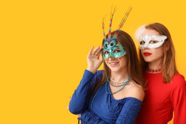 Sarı arka planda karnaval maskeli güzel genç kadınlar.