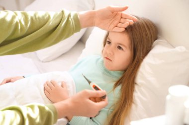 Anne, yatak odasında hasta kızının alnına termometreyle dokunuyor.