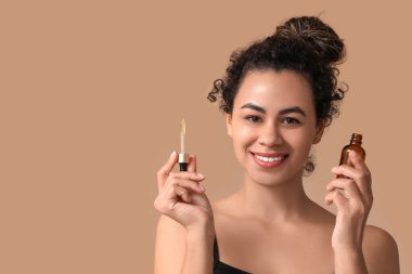 Kahverengi arka planda bir şişe kozmetik yağı olan güzel bir Afro-Amerikalı kadın.