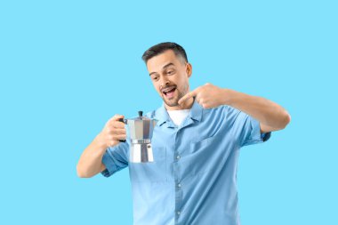 Yakışıklı adam mavi arka planda gayzer kahve makinesini işaret ediyor.