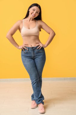Sarı arka planda yeni kotlu güzel, genç ve mutlu bir kadın. Kilo verme konsepti