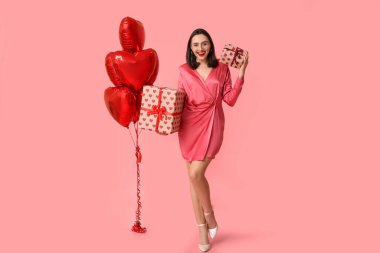 Hediye kutuları ve pembe arka planda kalp şeklinde balonları olan genç ve güzel bir kadın. Sevgililer Günü kutlaması