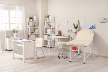 Masası, kanepesi ve çocuk çizimleri olan çocuk doktorunun bürosu.