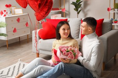 Young couple with bouquet of roses at home on Valentine's day