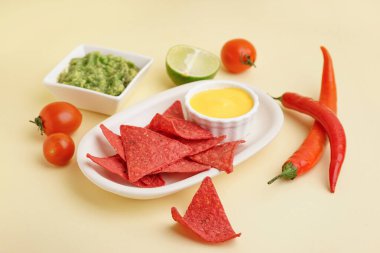 Sarı arka planda kırmızı nachos, sos ve biber tabağı.