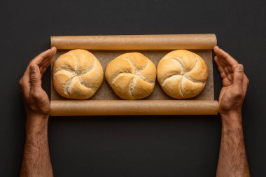 Taze lezzetli Kayzer dürümleri olan erkek eller siyah arka planda pişmiş kağıt üzerinde