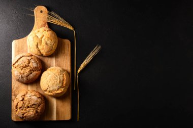 Lezzetli çörekleri ve siyah arka planda buğday kulakları olan bir tahta.