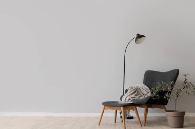 Gri duvarın yanında koltuk, ayak sehpası ve lamba olan oturma odasının içinde.