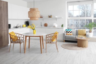 Masası, koltukları, çiçekleri, mimoza çiçekleri, tezgahları ve kanepesi olan modern şık bir mutfak stüdyosu.