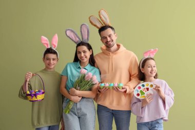 Yeşil arka planda Paskalya hediyeleri olan tavşan kulaklı mutlu bir aile.