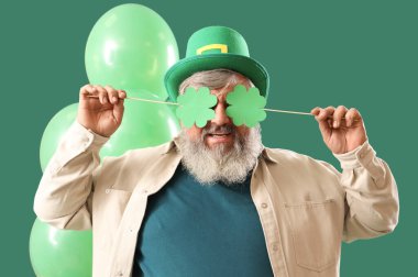 Yeşil arka planda kağıt yoncalar ve balonlar olan şapkalı olgun bir adam. Aziz Patrick Günü kutlaması