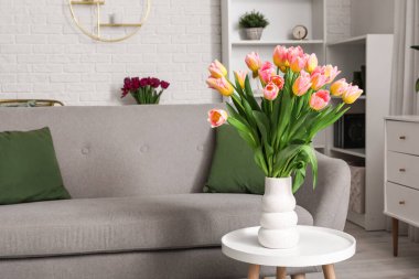 Oturma odasındaki kanepenin yanındaki masada güzel laleleri olan vazo.