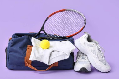 Toplu spor çantası, tenis raketi ve mor arka planda ayakkabılar.