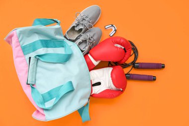 Ayakkabılı spor çantası ve turuncu arka planda boks eldivenleri.