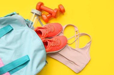 Spor giyimli spor çantası ve sarı arka planda spor malzemeleri.