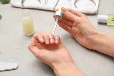 Gri grunge arka planda tırnaklarına tırnak yağı süren kadın elleri, yakın plan.