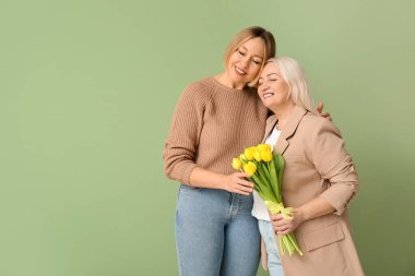 Annesiyle yetişkin bir kadın ve yeşil arka planda bir buket lale. Uluslararası Kadınlar Günü kutlamaları