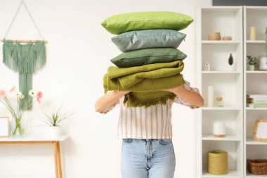 Odasında katlanmış sıcak ekoseli yastık yığını tutan kadın.