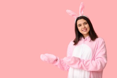 Tavşan kostümlü güzel bir kadın pembe arka plandaki bir şeyi işaret ediyor. Paskalya kutlaması