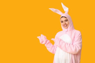 Tavşan kostümlü güzel bir kadın sarı arka plandaki bir şeyi işaret ediyor. Paskalya kutlaması