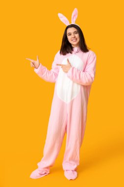 Tavşan kostümlü güzel bir kadın sarı arka plandaki bir şeyi işaret ediyor. Paskalya kutlaması