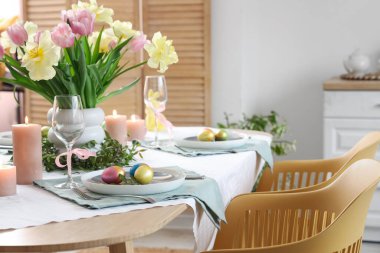 Çiçek, çatal bıçak, mum ve boyalı yumurta dolu Paskalya sofrası.