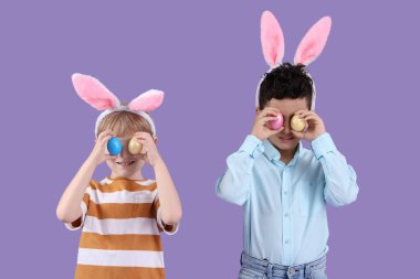 Mor arka planda Paskalya yumurtaları olan tavşan kulaklı şirin çocuklar.