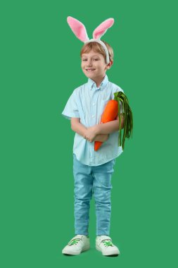 Yeşil arka planda oyuncak havucu olan tavşan kulaklı şirin bir çocuk. Paskalya kutlaması