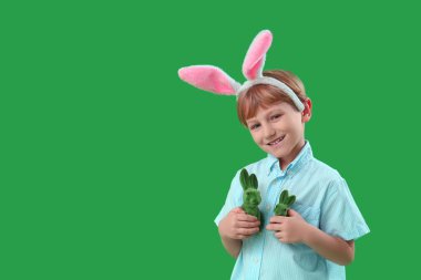 Yeşil arka planda oyuncak tavşanı olan tavşan kulaklı şirin bir çocuk. Paskalya kutlaması