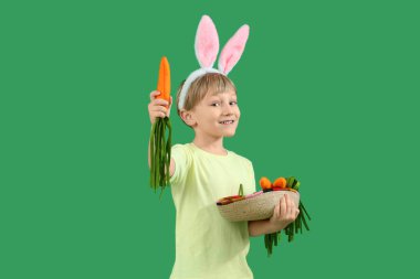 Yeşil arka planda oyuncak havucu olan tavşan kulaklı şirin bir çocuk. Paskalya kutlaması