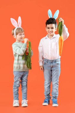 Turuncu arka planda oyuncak havuçları olan tavşan kulaklı şirin çocuklar. Paskalya kutlaması