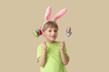 Bej arka planda Paskalya yumurtaları olan tavşan kulaklı şirin bir çocuk.