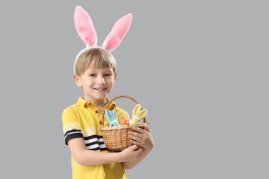 Tavşan kulaklı şirin çocuk elinde sepet ve gri arka planda oyuncak tavşan tutuyor. Paskalya kutlaması