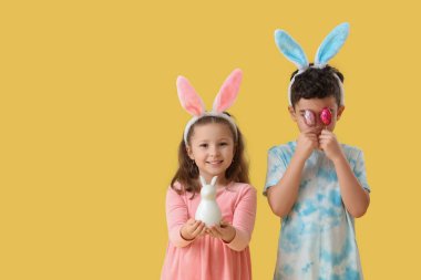 Tavşan kulaklı şirin çocuklar Paskalya yumurtası ve sarı arka planda oyuncak tavşan.