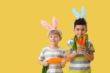 Sarı arka planda oyuncak havuçları olan tavşan kulaklı şirin çocuklar. Paskalya kutlaması