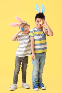 Sarı arka planda Paskalya yumurtaları olan tavşan kulaklı şirin çocuklar.
