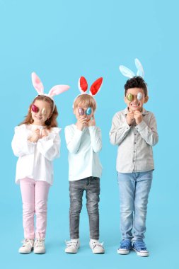 Mavi arka planda Paskalya yumurtaları olan tavşan kulaklı şirin çocuklar.