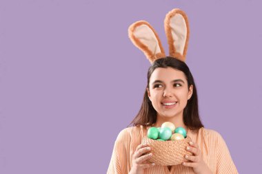 Tavşan kulaklı güzel bir kadın elinde hasırdan bir kaseyle Paskalya yumurtası tutuyor.