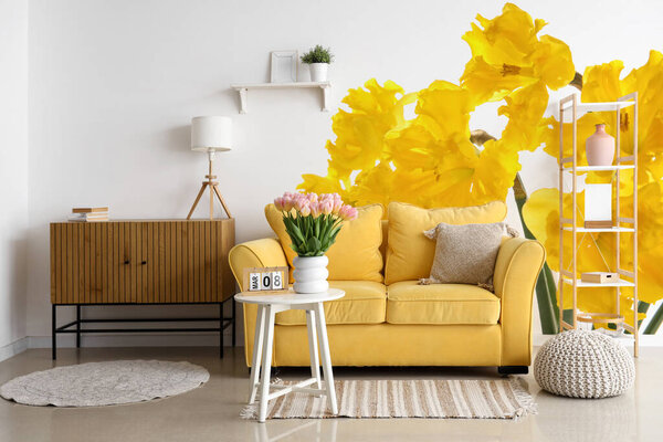 Stylish interior of room with yellow sofa and beautiful daffodil flowers on wall