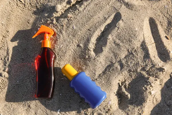 Creative composition with bottles of sunscreen cream on sand at sea beach