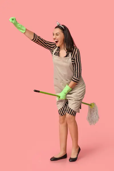 Портрет Счастливой Молодой Домохозяйки Фартуке Летящей Швабру Розовом Фоне — стоковое фото